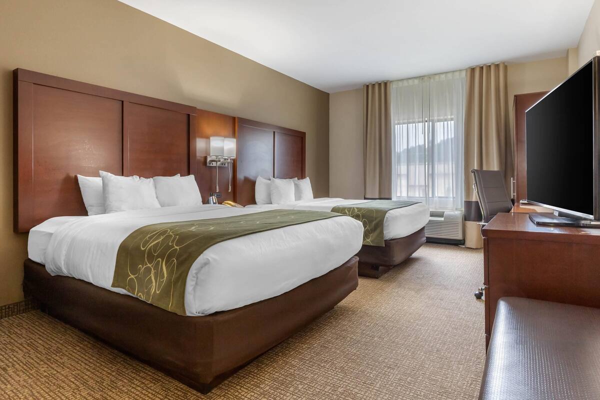 Habitación de hotel con dos camas, un escritorio, un televisor y un aire acondicionado.