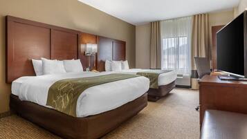 A hotel room with two beds, a desk, a television, and an air conditioning unit.
