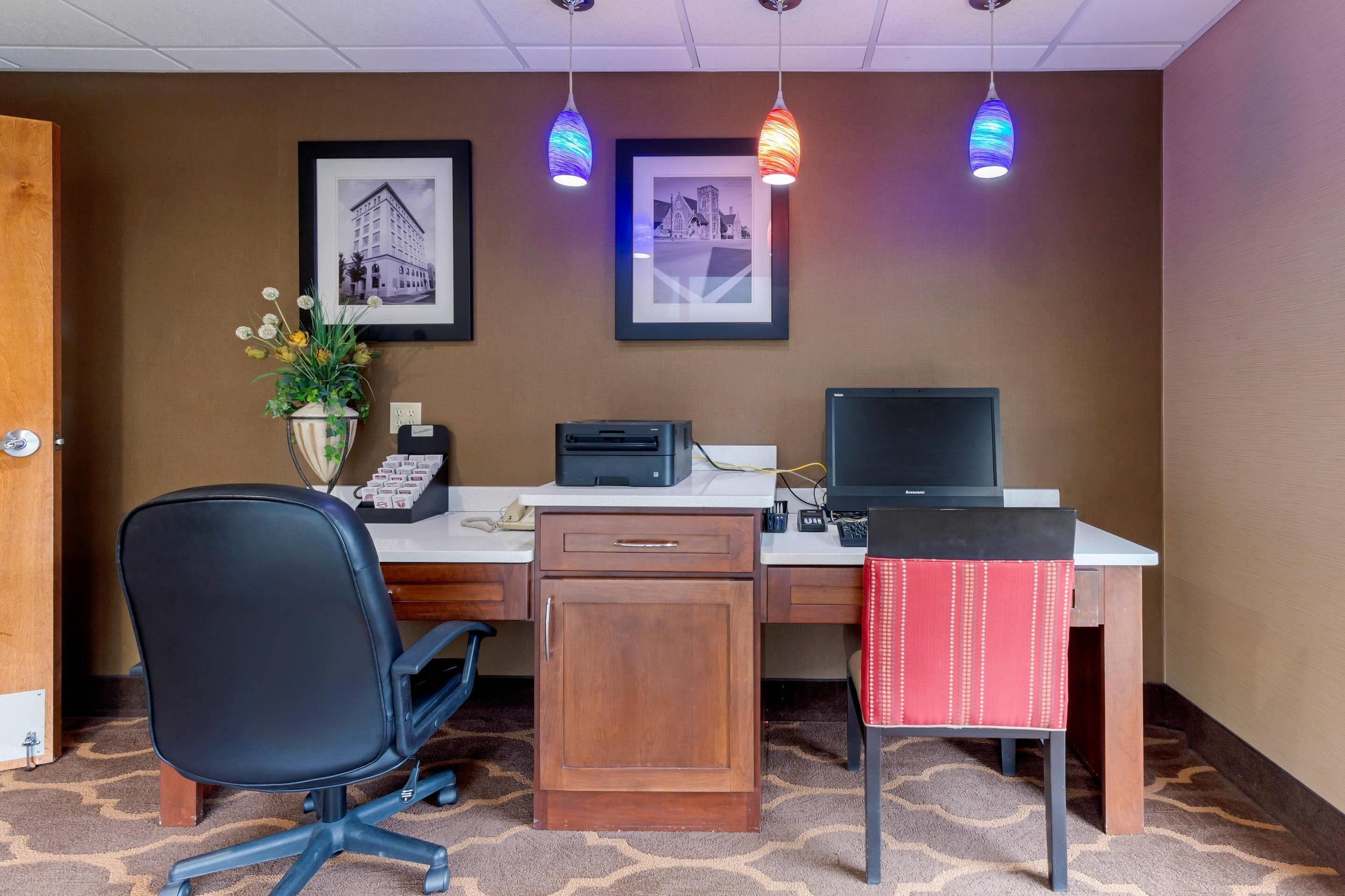 A hotel room with a desk, chair, printer, and framed pictures on the wall.