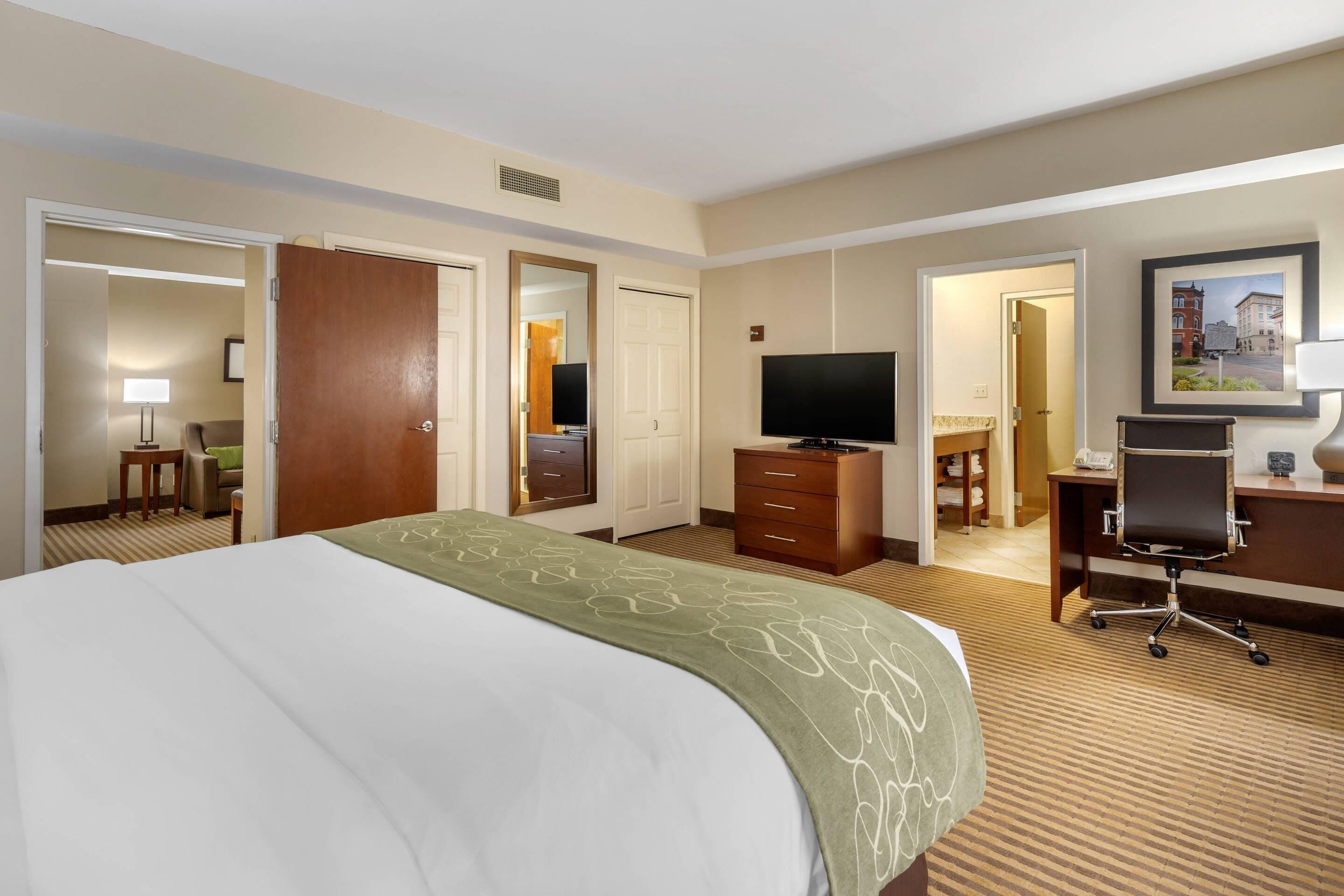 A hotel room with a bed, a television, a desk with a chair, and a bathroom visible through an open door.