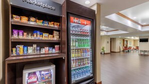 Una zona de kitchenette con un refrigerador lleno de bebidas, un microondas y una estantería con aperitivos.