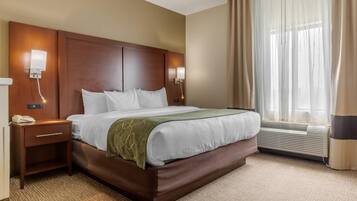 Habitación de hotel con una cama grande, lámparas de noche, teléfono, ventana con cortinas y equipo de aire acondicionado.