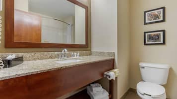 Un baño con lavamanos de encimera de granito, tocador de madera, inodoro blanco y dos cuadros en la pared.