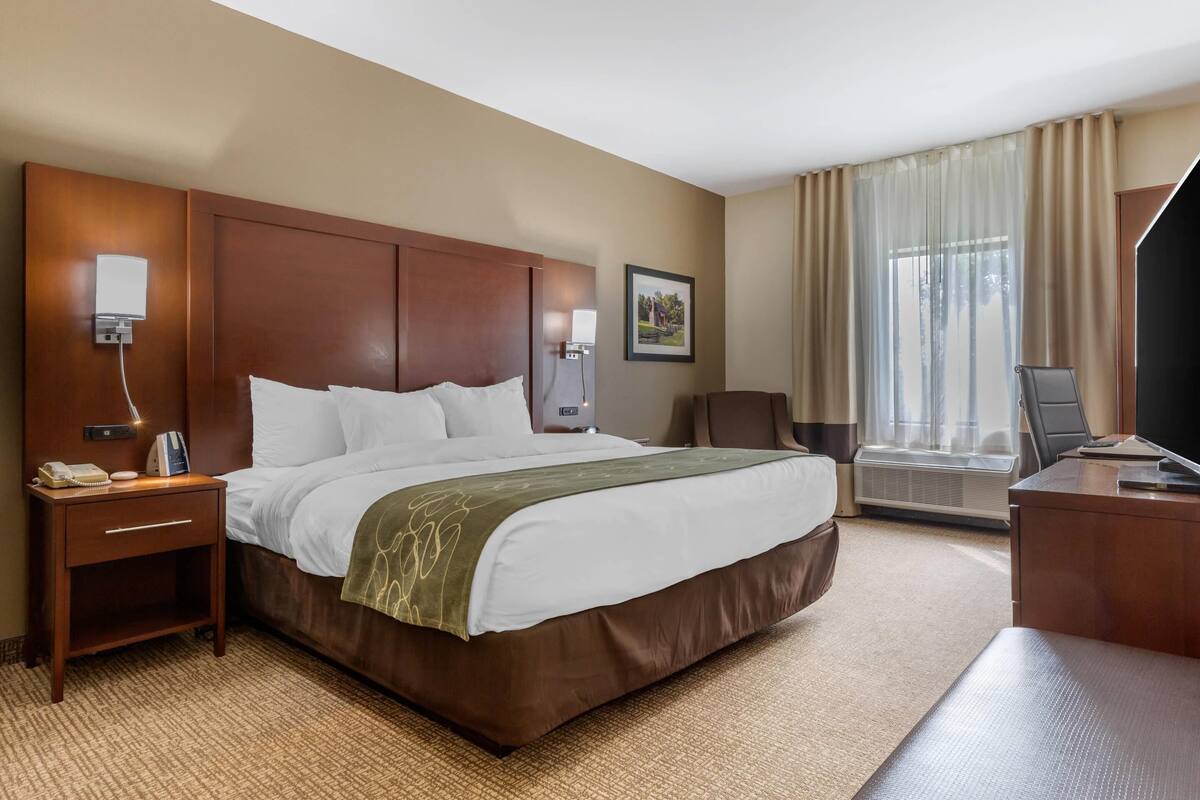 Habitación de hotel con una cama grande, mesitas de noche, escritorio, una silla, televisor y ventana con cortinas.