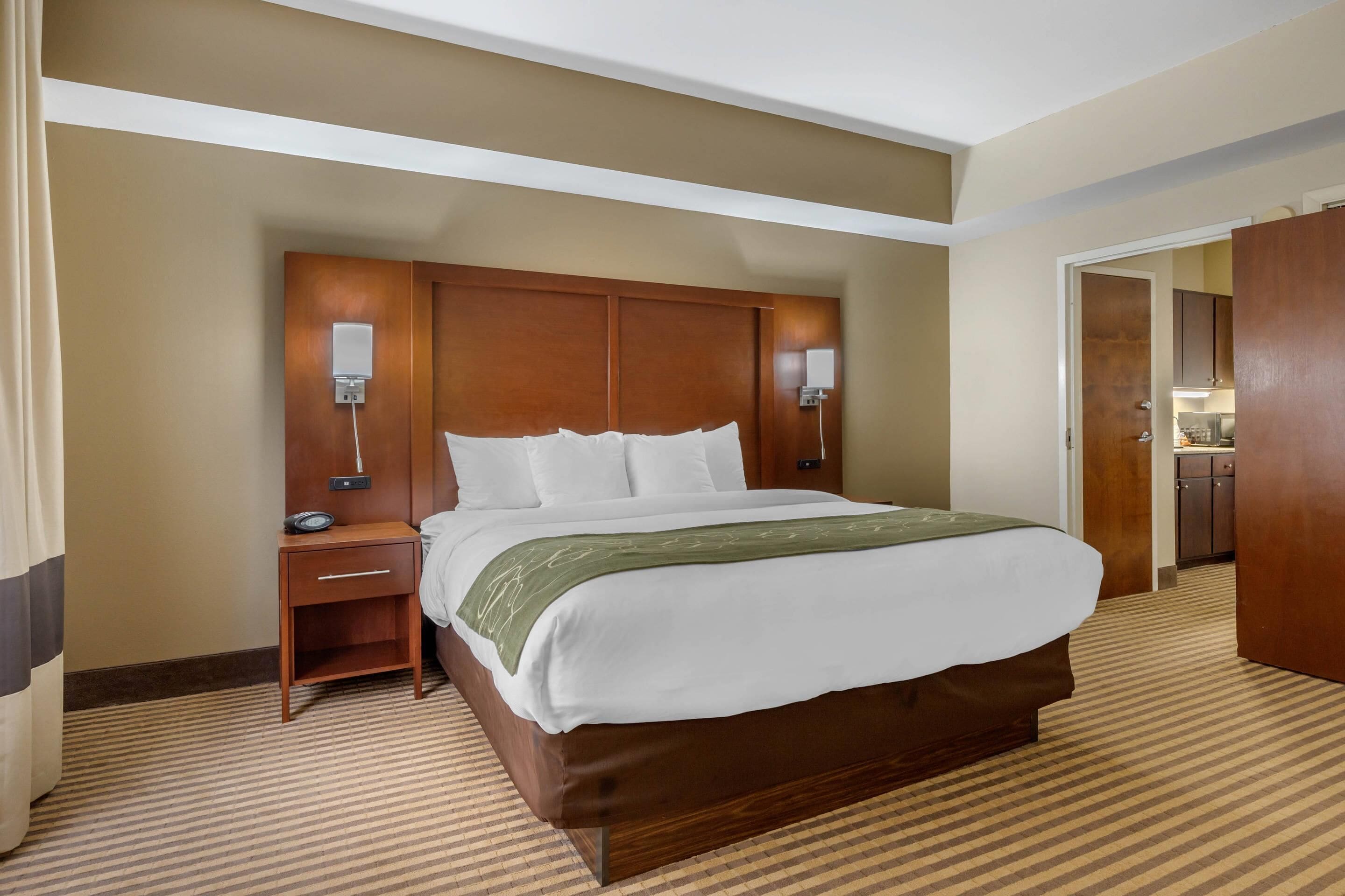 A hotel room with a large bed, a nightstand, a lamp, and a wooden wardrobe.