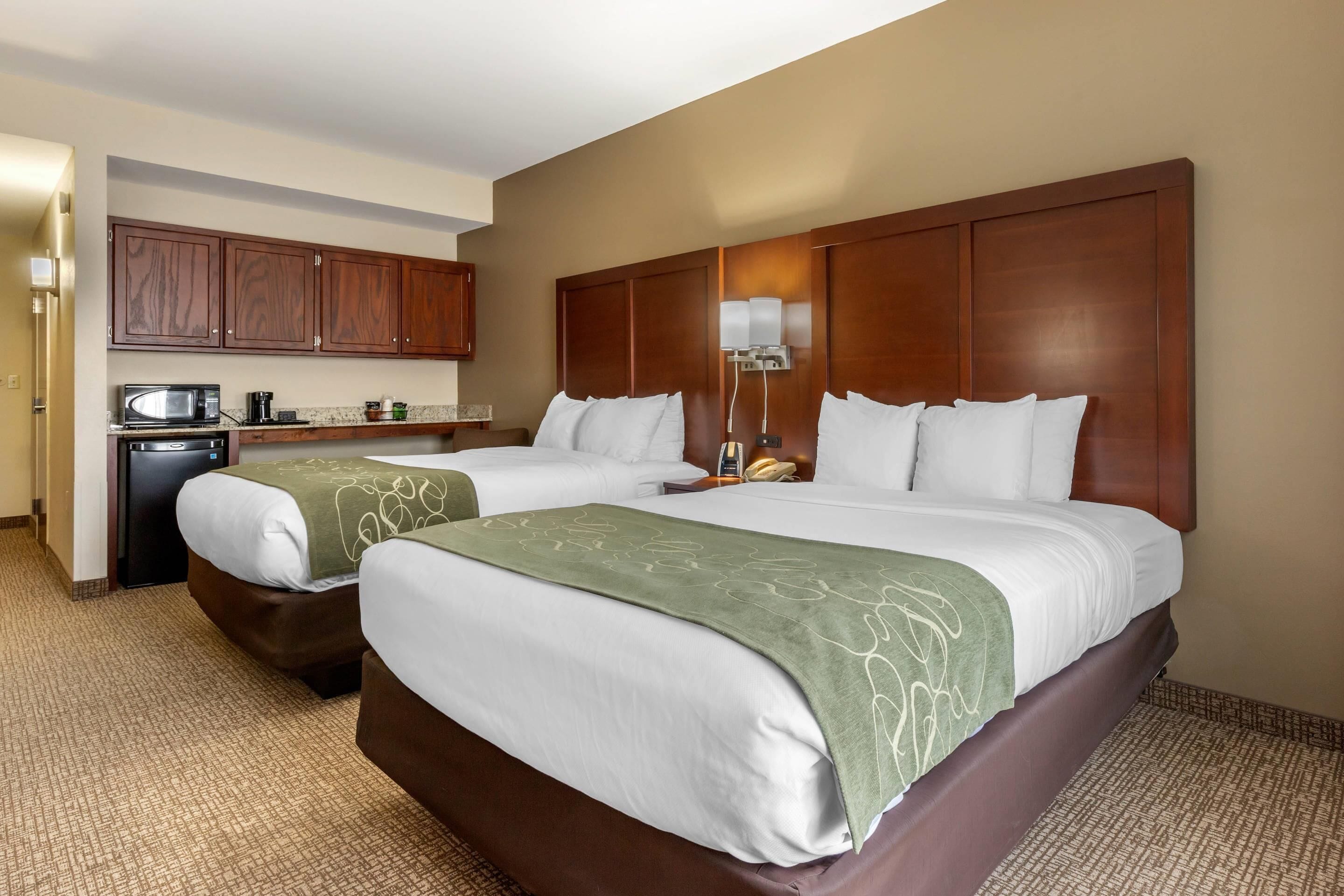 A hotel room with two beds, a kitchenette, and a large wooden headboard.