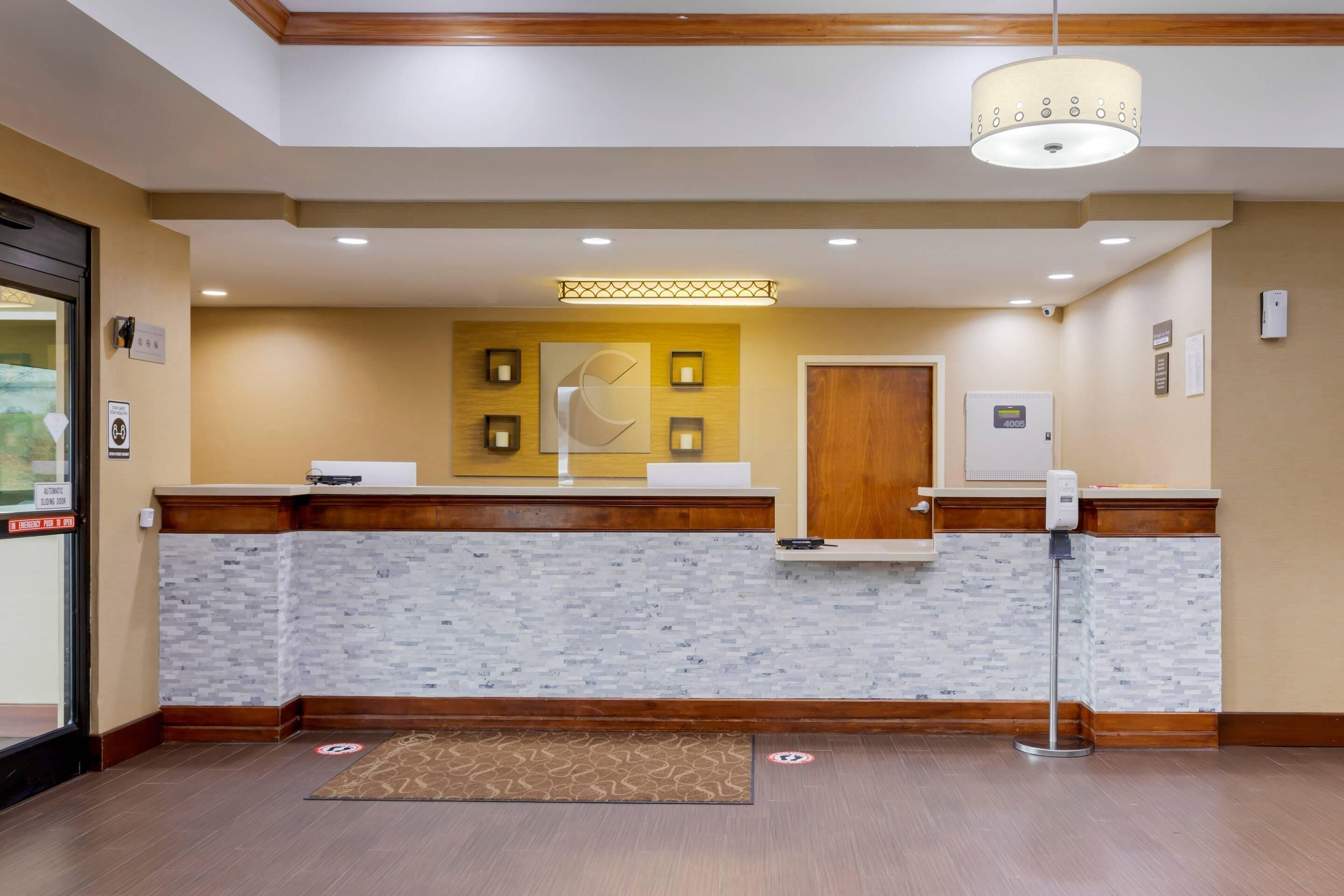 A reception area with a wooden counter, a reception desk, a wall-mounted light fixture, and a door.