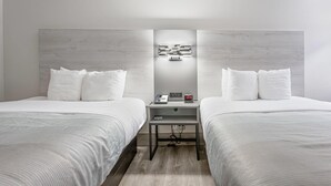 A hotel room with two beds, a bedside table with a phone and a digital clock, and a wall-mounted light fixture. - Quality Inn Prattville I-65 (Prattville)