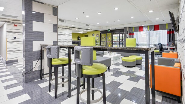 A modern bar area with high stools and orange seating, featuring a checkered floor and contemporary decor. - Quality Inn Prattville I-65 (Prattville)
