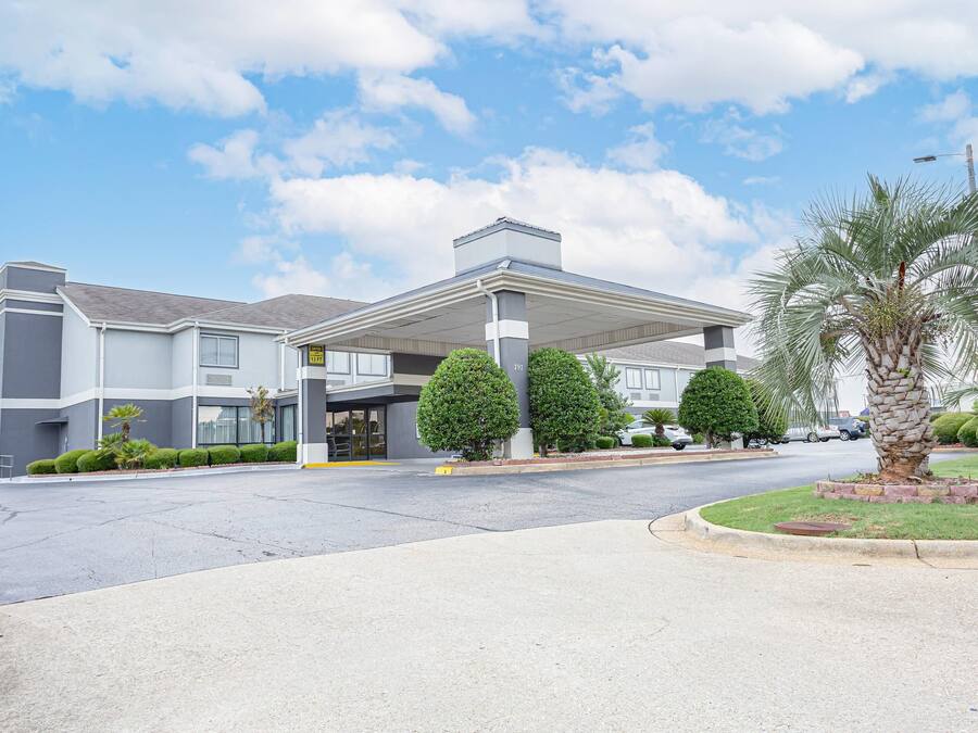 A modern hotel with a covered entrance, a parking lot, and well-maintained landscaping including palm trees and shrubs.