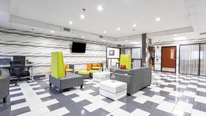 A modern lobby with a checkered floor, grey and yellow seating, a flat-screen TV, and a reception desk. - Quality Inn Prattville I-65 (Prattville)