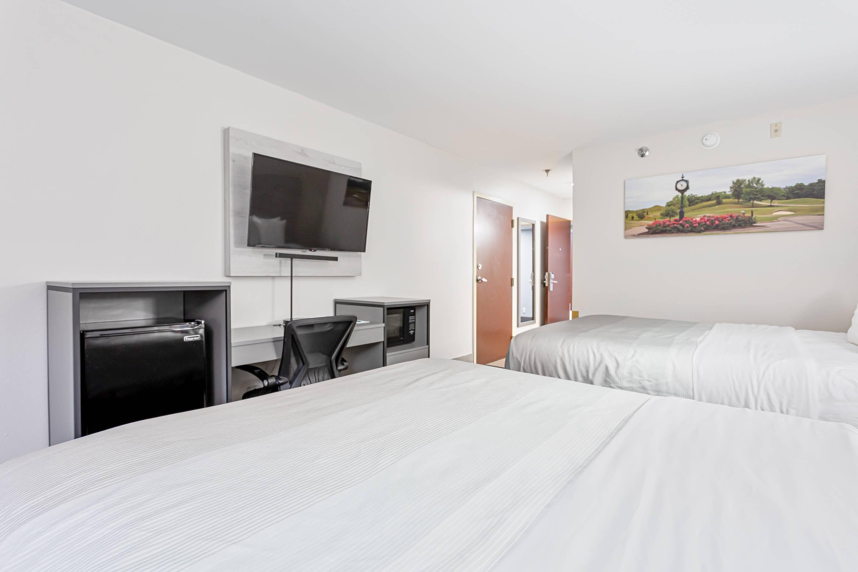A hotel room with two beds, a desk with a computer, a TV, and a painting of a golf course.