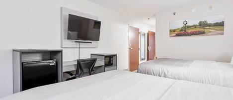 A hotel room with two beds, a desk with a computer, a TV, and a painting of a golf course.