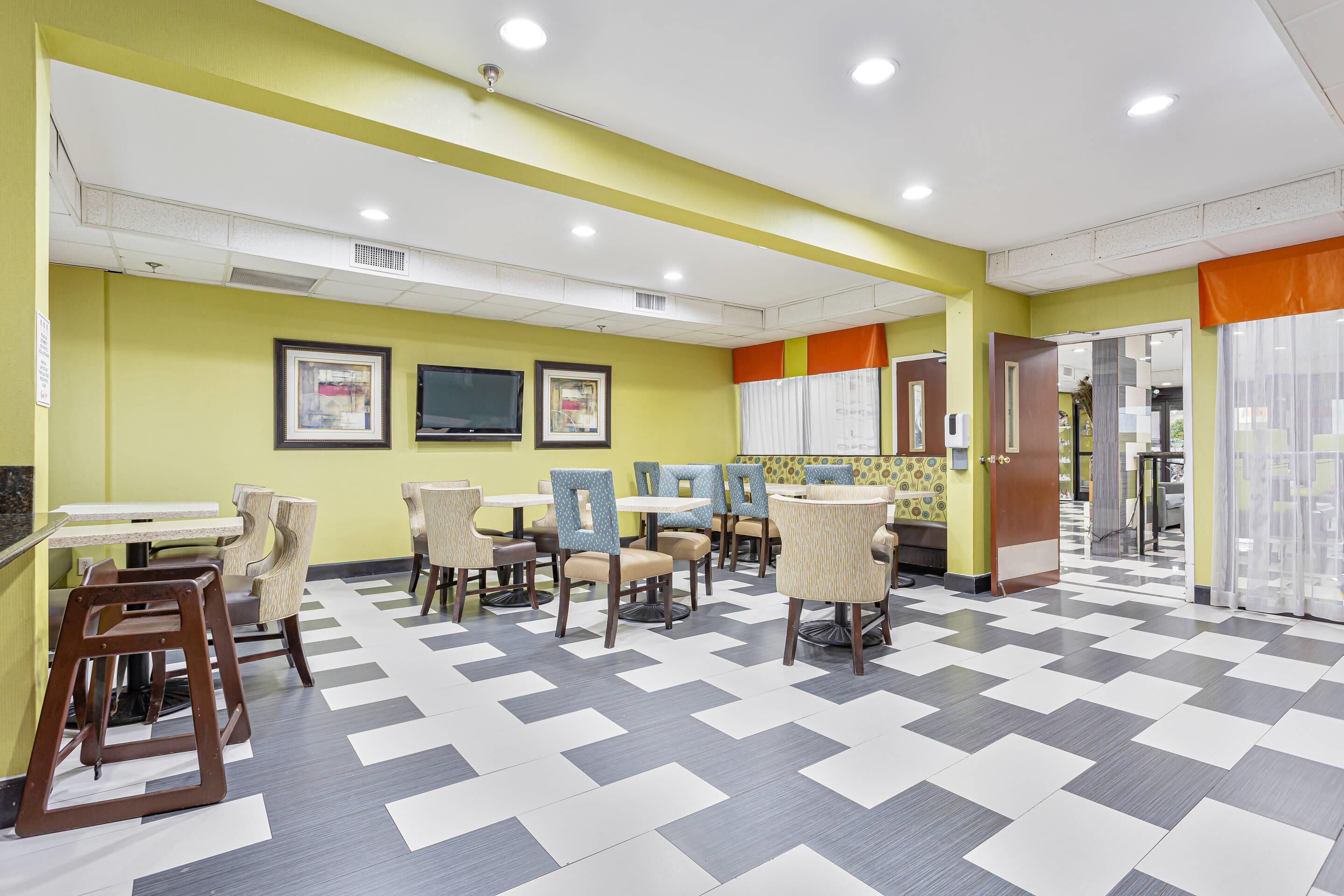 A brightly lit indoor space with yellow walls, a checkered floor, and multiple seating areas with tables and chairs.
