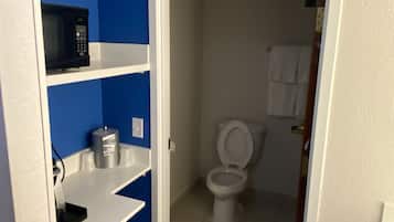A bathroom with a white toilet, a blue wall, and a white sink with a microwave above it.