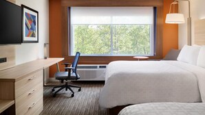 A hotel room with a bed, desk, chair, and a large window offering a view of trees.