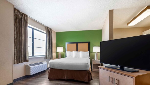 A hotel room with a bed, a TV, a heater, and a window with curtains. - Extended Stay America Select Suites Denver Tech Center South (Englewood)