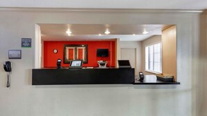 A reception desk with a red wall, a clock, a phone, and a computer. - Extended Stay America Select Suites Denver Tech Center South (Englewood)