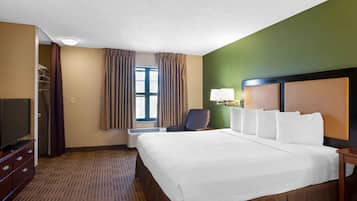 Habitación de hotel con una cama grande, televisión, una silla y ventana con cortinas.