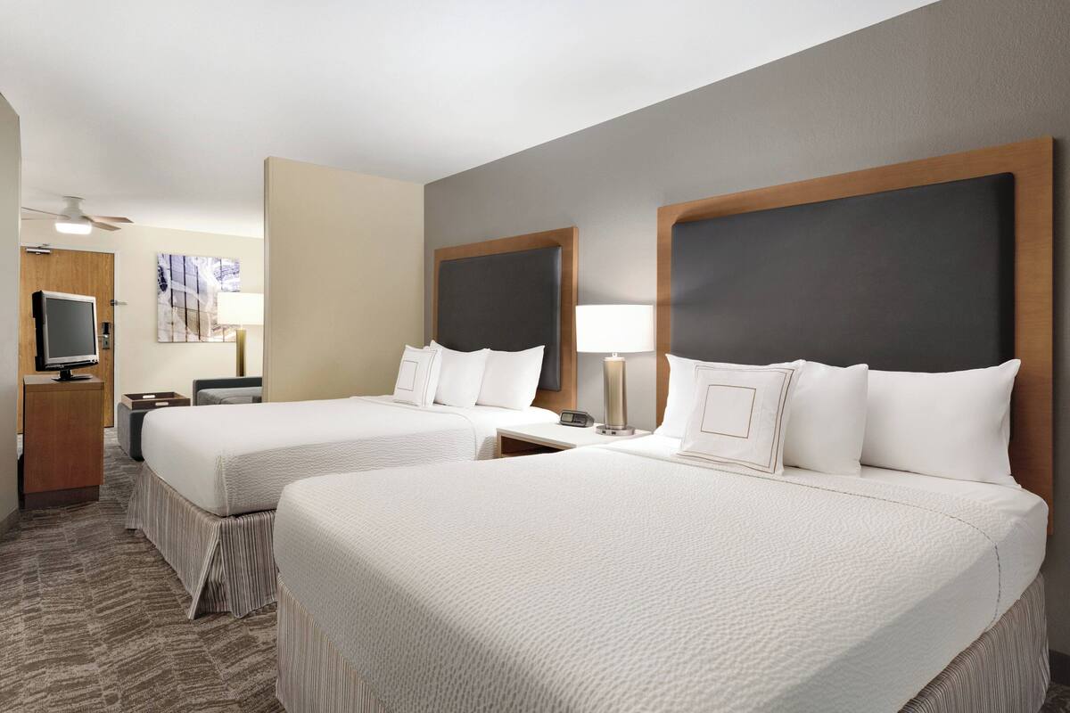 A hotel room with two beds, a desk, a TV, and a lamp.