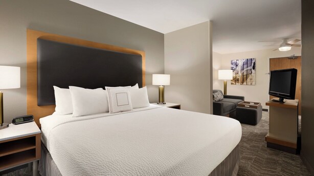 A hotel room with a large bed, bedside tables, a desk, a television, and a seating area with a sofa and ottoman. - SpringHill Suites Phoenix North (Phoenix)