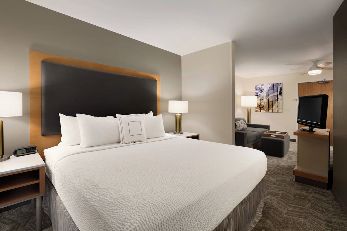 A hotel room with a large bed, bedside tables, a desk, a television, and a seating area with a sofa and ottoman.