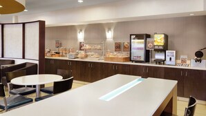 A modern hotel breakfast area with a long counter, seating, and various food and beverage dispensers. - SpringHill Suites Phoenix North (Phoenix)