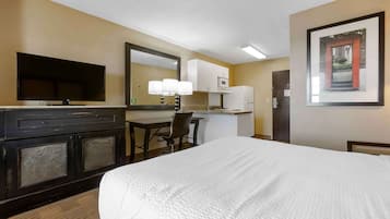 A hotel room with a large bed, a TV, a desk with a chair, a microwave, and a refrigerator.