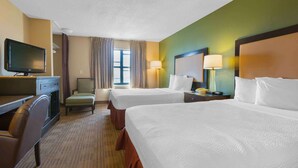 A hotel room with two beds, a desk with a TV, a chair, and a window with curtains.