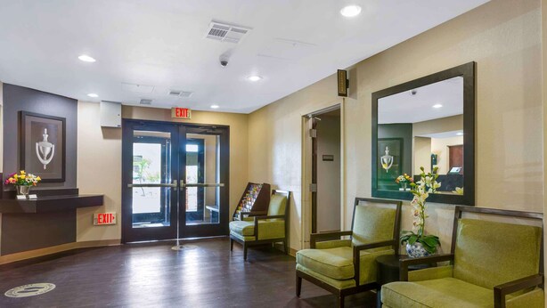 A reception area with a desk, chairs, an exit sign, and a mirror.