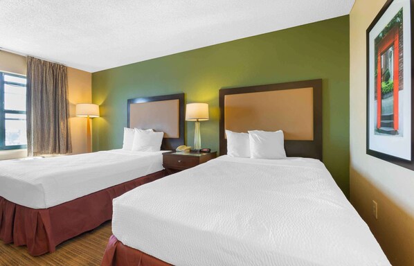 A hotel room with two beds, a nightstand, a lamp, and a window with curtains.