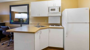 A compact kitchen with white cabinets, a microwave, a refrigerator, a sink, and a chair.