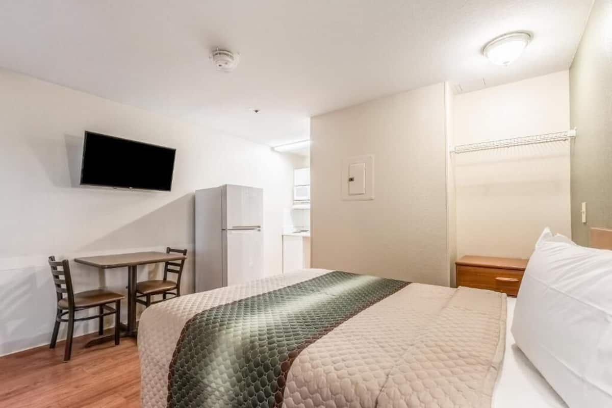 Ein Hotelzimmer mit einem Bett, einem Schreibtisch, einem Stuhl, einem an der Wand montierten Fernseher und einem Kleiderschrank.