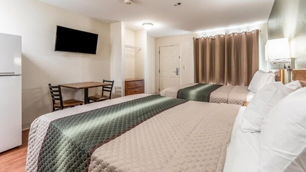 A hotel room with two beds, a desk, a chair, a television, and a bathroom door. - Studio 51 Extended Stay Hotel (Phoenix)