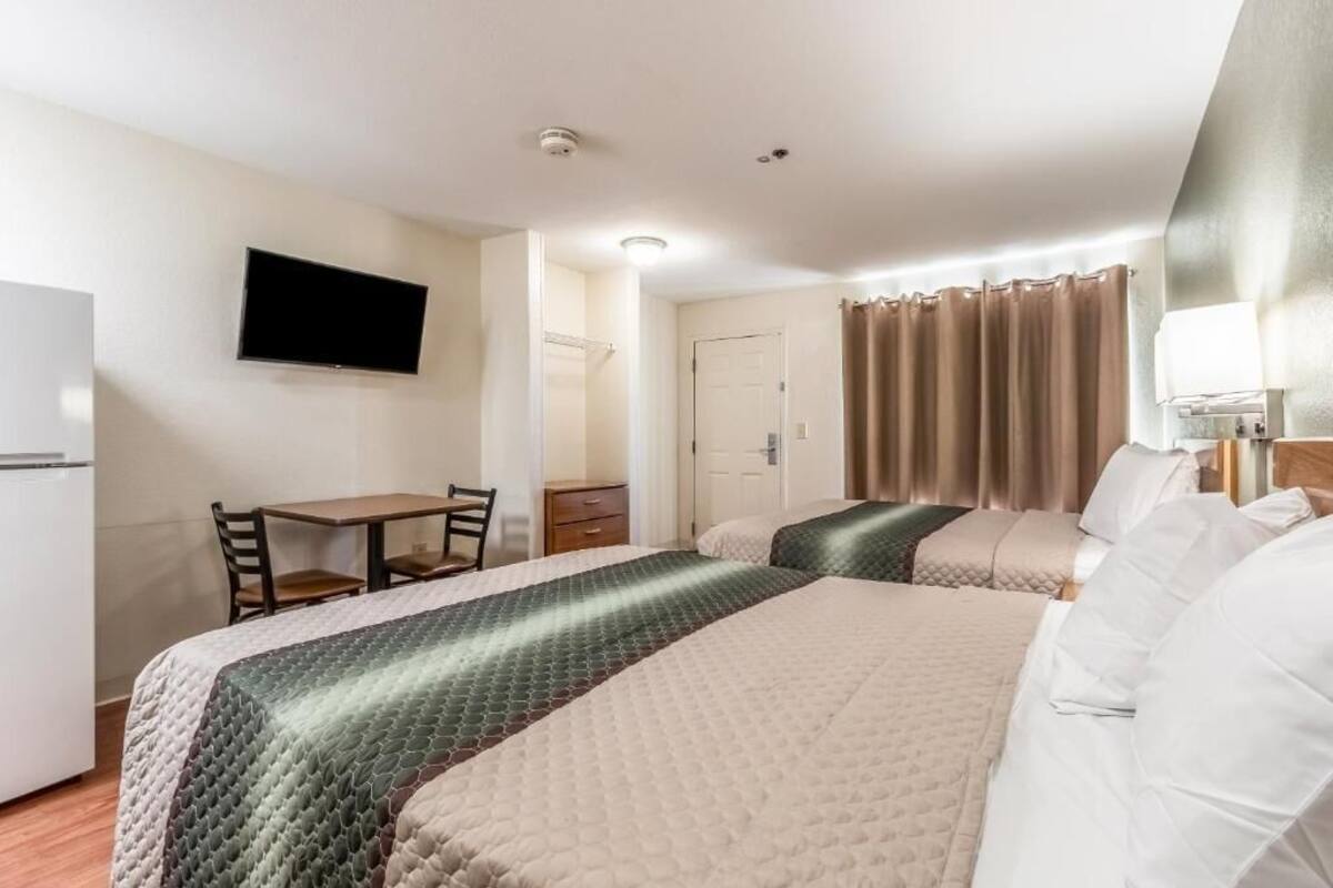 Ein Hotelzimmer mit zwei Betten, einem Schreibtisch, einem Sessel, einem Fernseher und einer Badezimmertür.