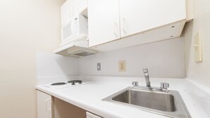 A kitchen with white cabinets, a stainless steel sink, and a built-in range hood. - Studio 51 Extended Stay Hotel (Phoenix)