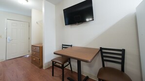 A small room with a wooden table and two chairs, a television mounted on the wall, and a door. - Studio 51 Extended Stay Hotel (Phoenix)