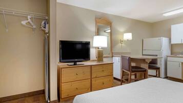 Ein Hotelzimmer mit Bett, Fernseher, Schreibtisch mit Stuhl, Kühlschrank und Spiegel.