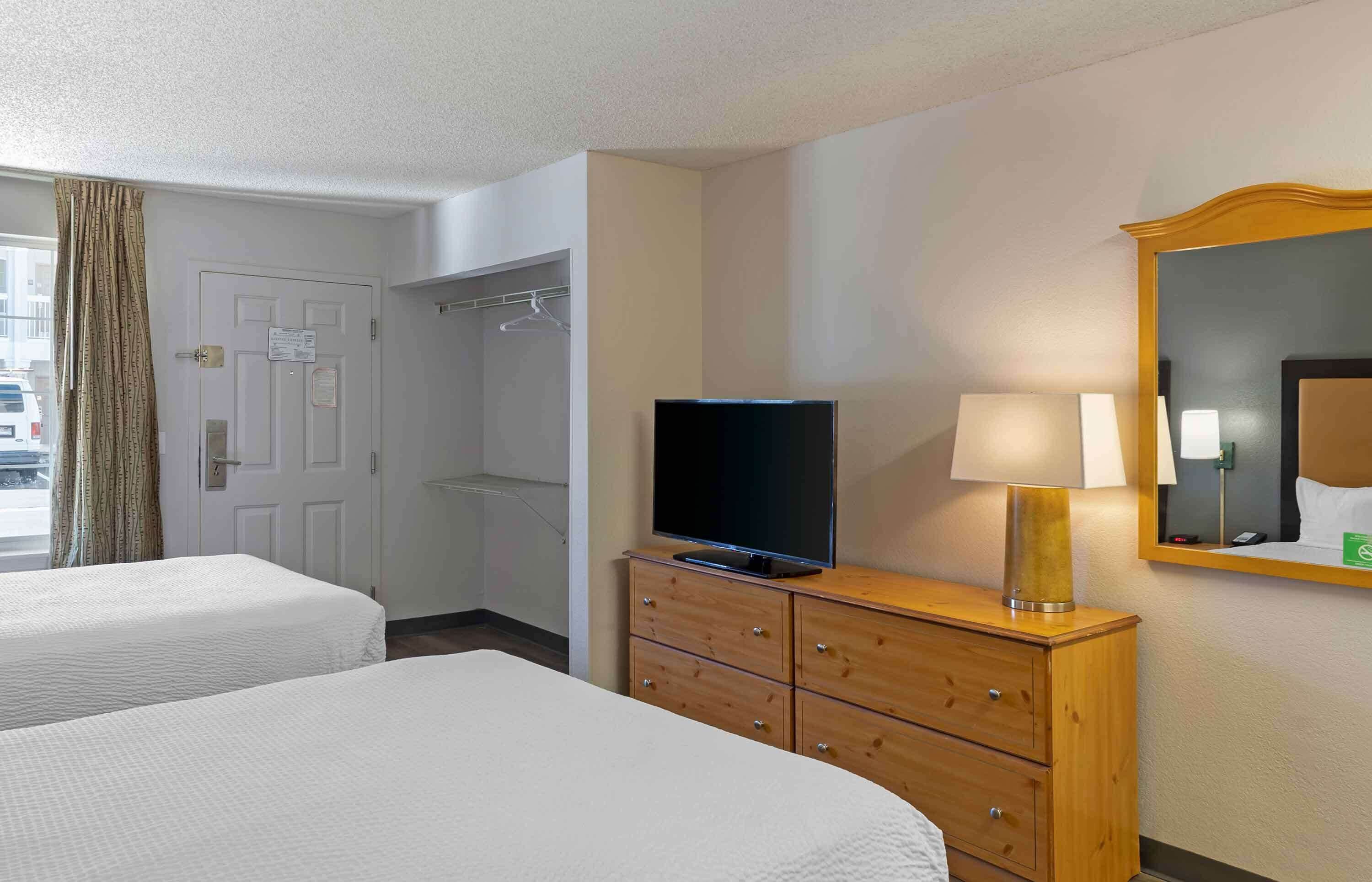 A hotel room with two beds, a television, a dresser, a mirror, and a window with curtains.