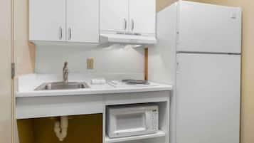 Una cocina compacta con armarios blancos, un lavamanos de acero inoxidable, un microondas y un refrigerador blanco.