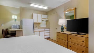 Habitación de hotel con cama, televisión, escritorio con computadora, refrigerador, microondas, lámpara y espejo.