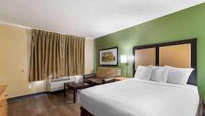 A hotel room with a large bed, a desk, a chair, a lamp, and a window with curtains. - Extended Stay America Select Suites Denver Cherry Creek (Glendale)