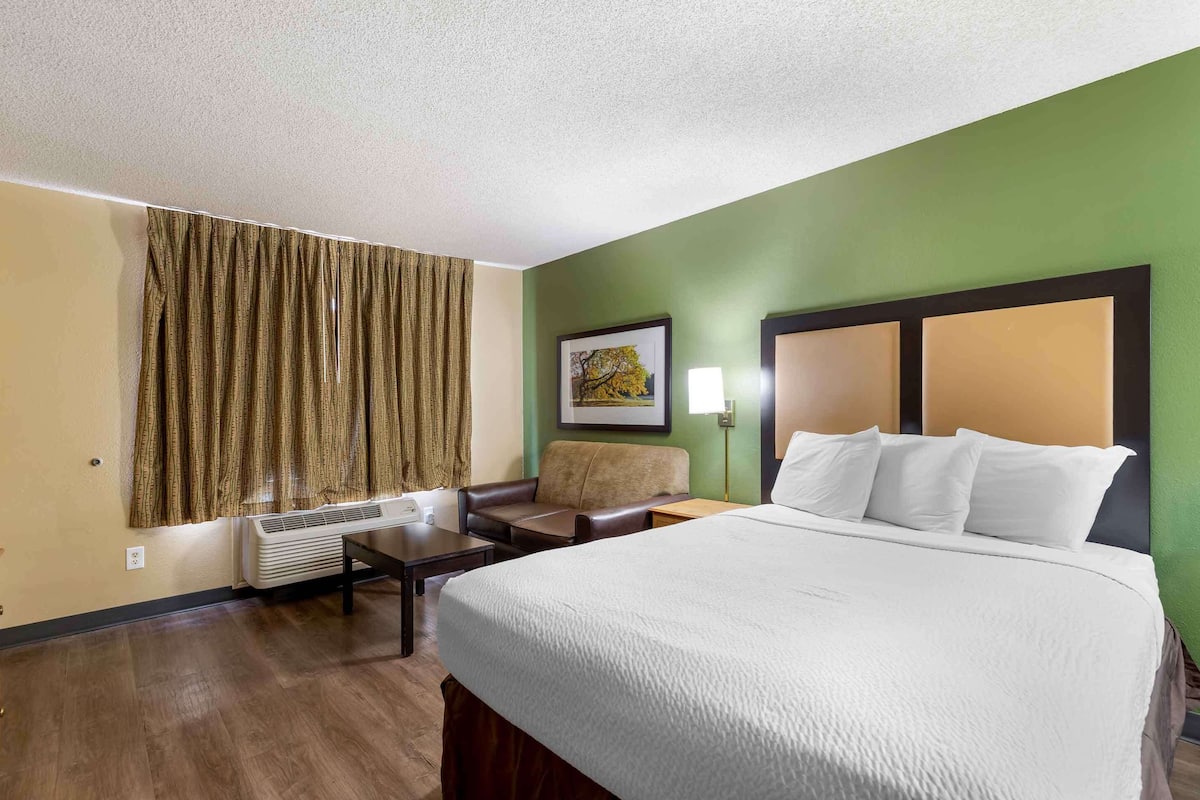 A hotel room with a large bed, a chair, a table, a lamp, and a picture on the wall.