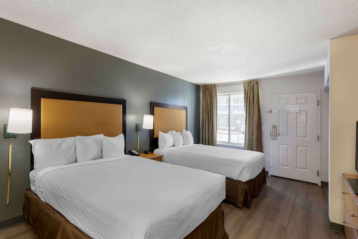 A hotel room with two beds, a TV, a desk, and a window with curtains.