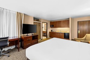 Een hotelkamer met een bed, bureau, televisie, kitchenette en een stoel.