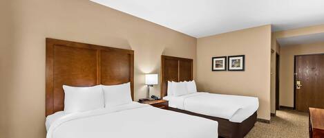 A hotel room with two beds, a nightstand with a lamp, and a door leading to another room.