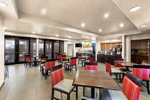 A spacious indoor dining area with multiple tables and chairs, a kitchen area, and large windows.