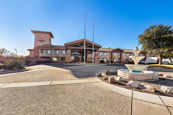 A Comfort Inn hotel with a central entrance, a flagpole, and a decorative fountain.