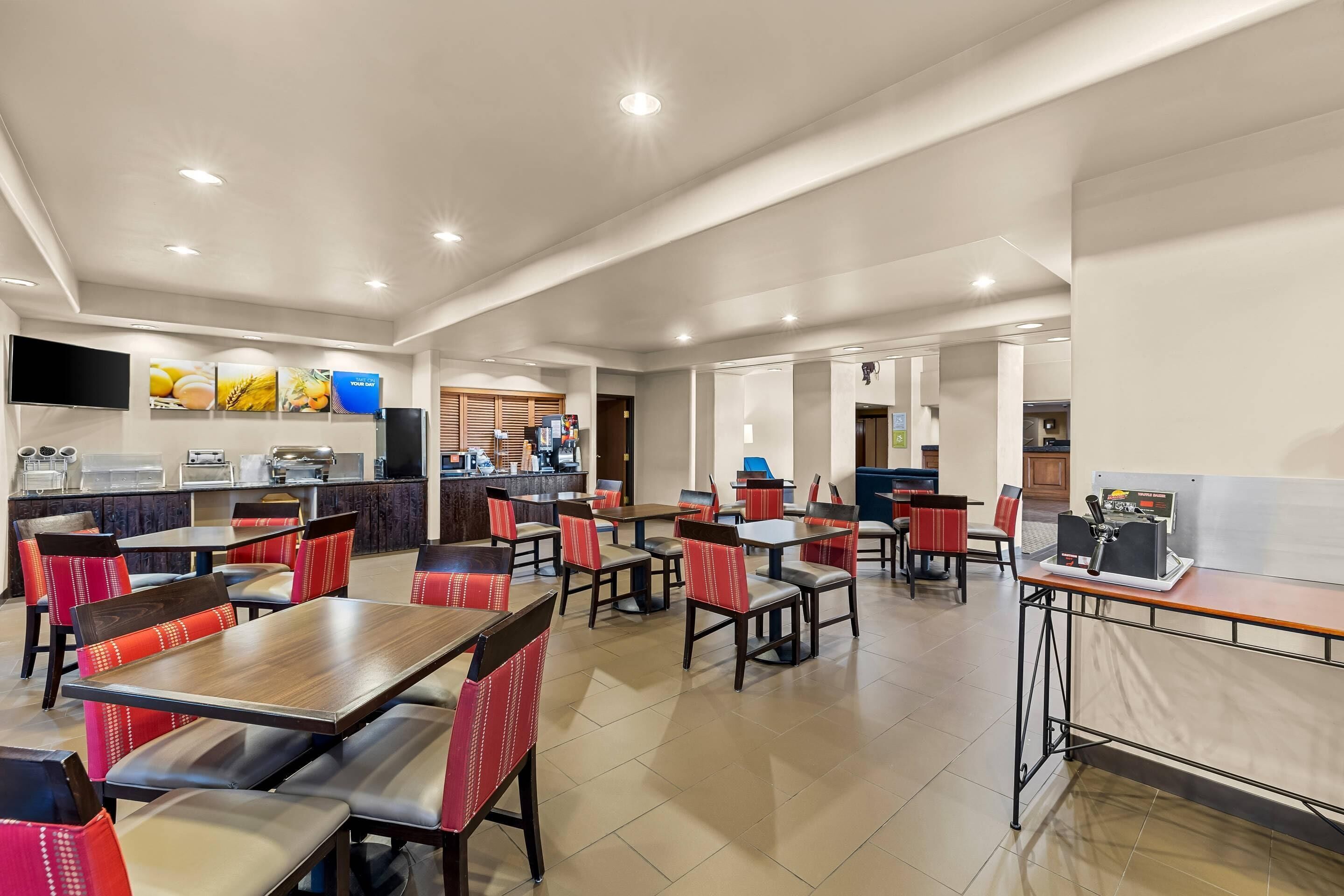 A spacious restaurant with multiple dining tables and chairs, a kitchen area, and a flat-screen TV mounted on the wall.