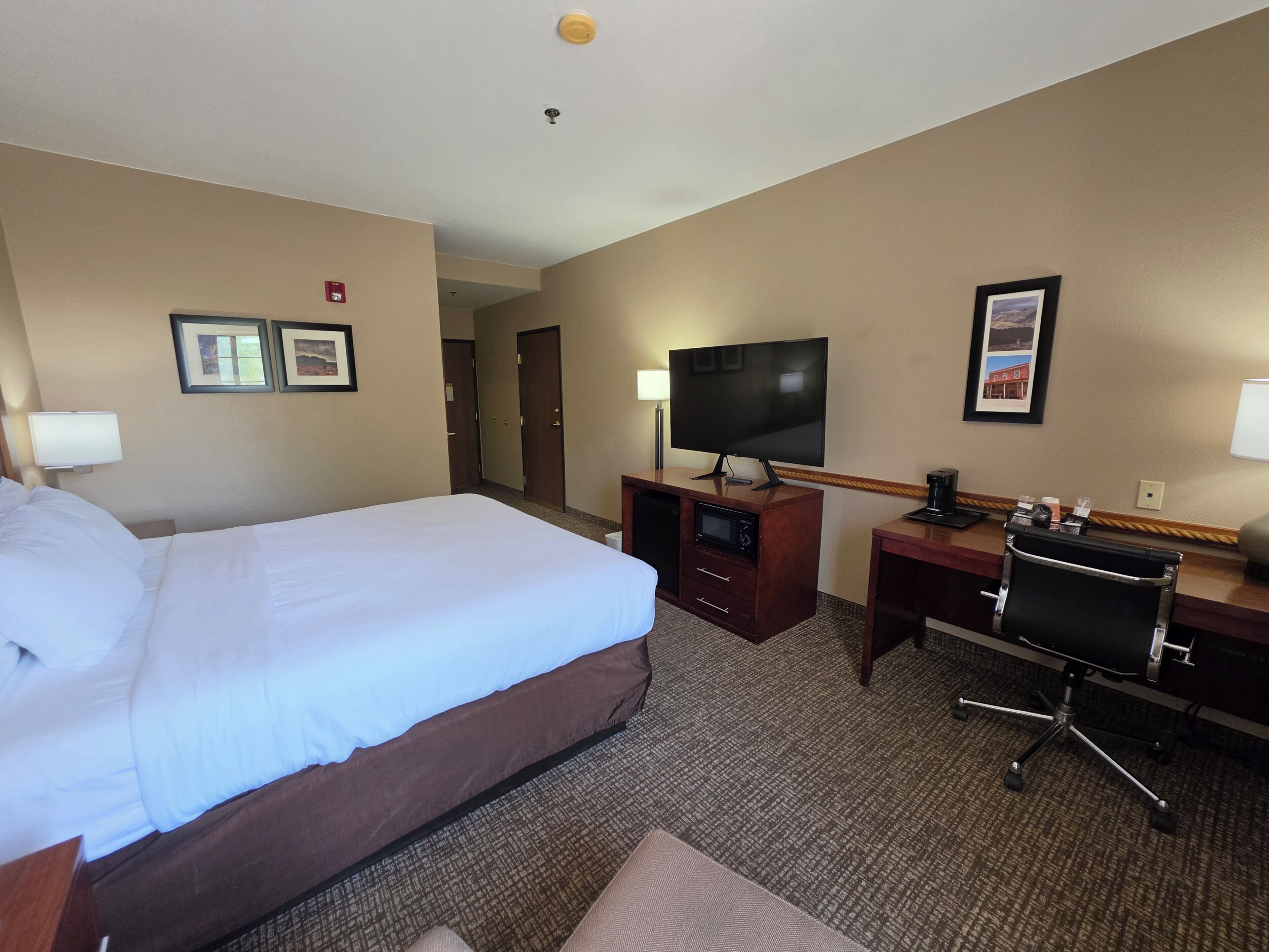 Une chambre d’hôtel comprenant un lit, un bureau avec une télévision, une chaise et une lampe de bureau.